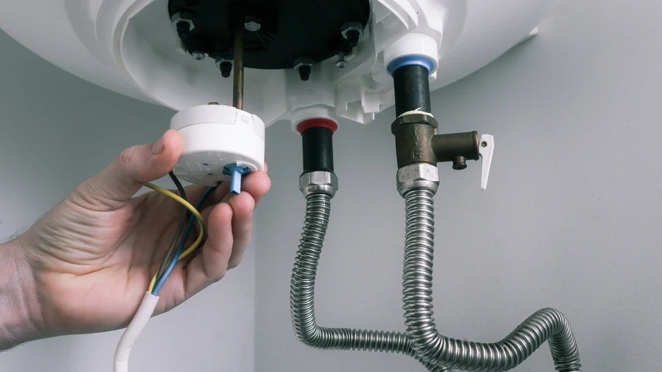 Intérieur résidentiel, technicien installant un chauffe-eau électrique au plafond, manipulation des raccordements électriques avec câbles apparents